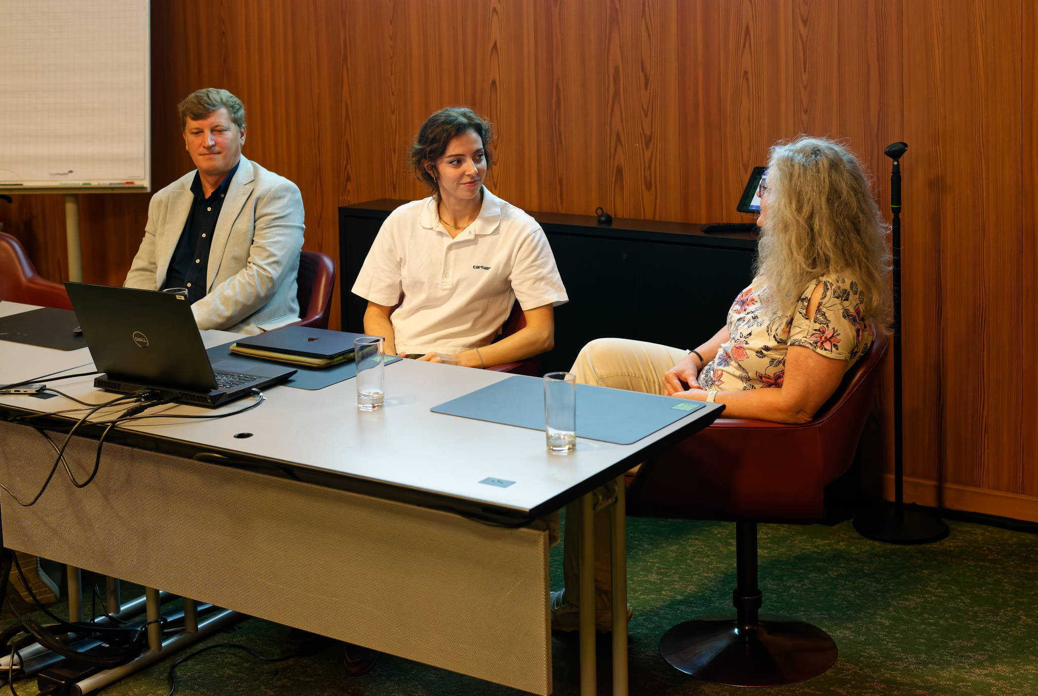 three people at a table with flipchart behind them and a laptop in front of them